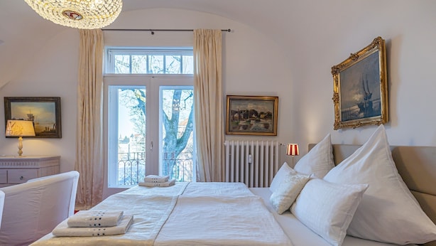 A hotel room with a large bed, a window with curtains, a radiator, and two framed pictures on the wall. - fewo1846 - Suite Royal - elegant old building apartment with balcony (Flensburg)