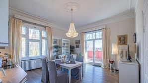A spacious living area with a dining table, chairs, a chandelier, and large windows. - fewo1846 - Suite Royal - elegant old building apartment with balcony (Flensburg)
