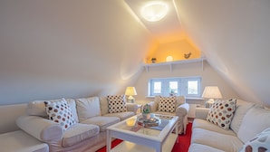 A modern living room with a red carpet, white furniture, and a sloped ceiling with a skylight. - fewo1846 - Villa Royal (Flensburg)