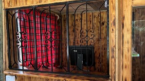 Une cabane en bois avec une fenêtre, un rideau à carreaux rouges et un radiateur noir.