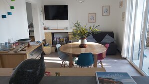 Una sala moderna con una mesa redonda de madera, sillas coloridas, un televisor de pantalla plana y un sofá con cojines.