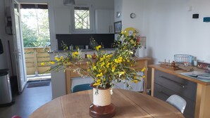 Un comedor con una mesa redonda de madera, un jarrón con flores amarillas y vistas a la cocina y al área exterior.
