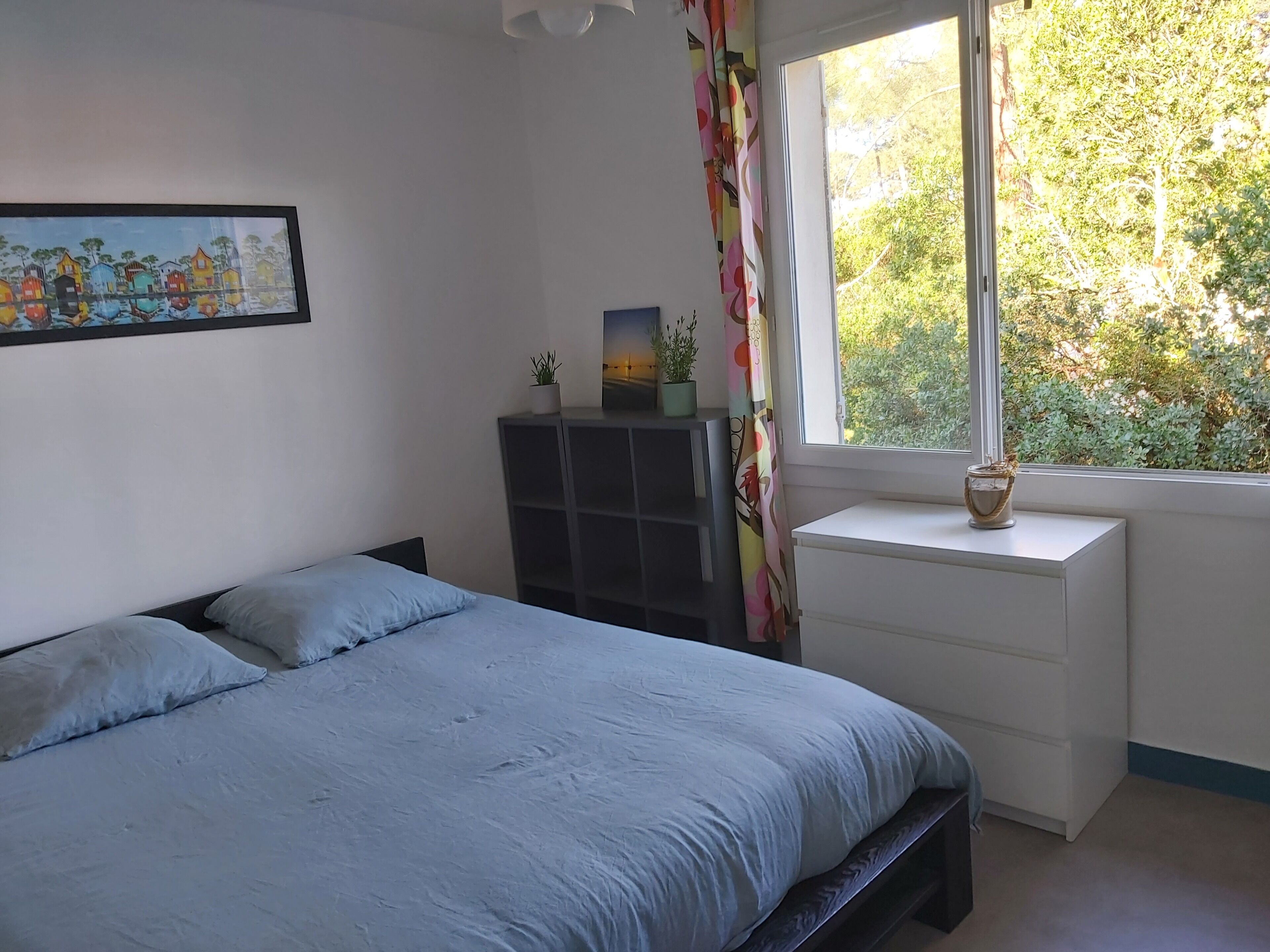 Un dormitorio con cama, mesita de noche, cómoda y ventana con vistas a la vegetación.