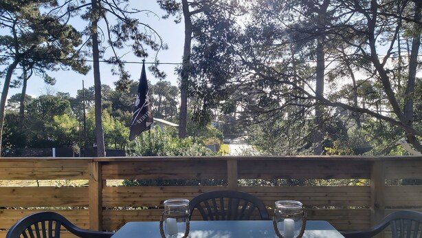 Una mesa al aire libre con dos candelabros de vidrio, rodeada de sillas, frente a una valla de madera y árboles al fondo.