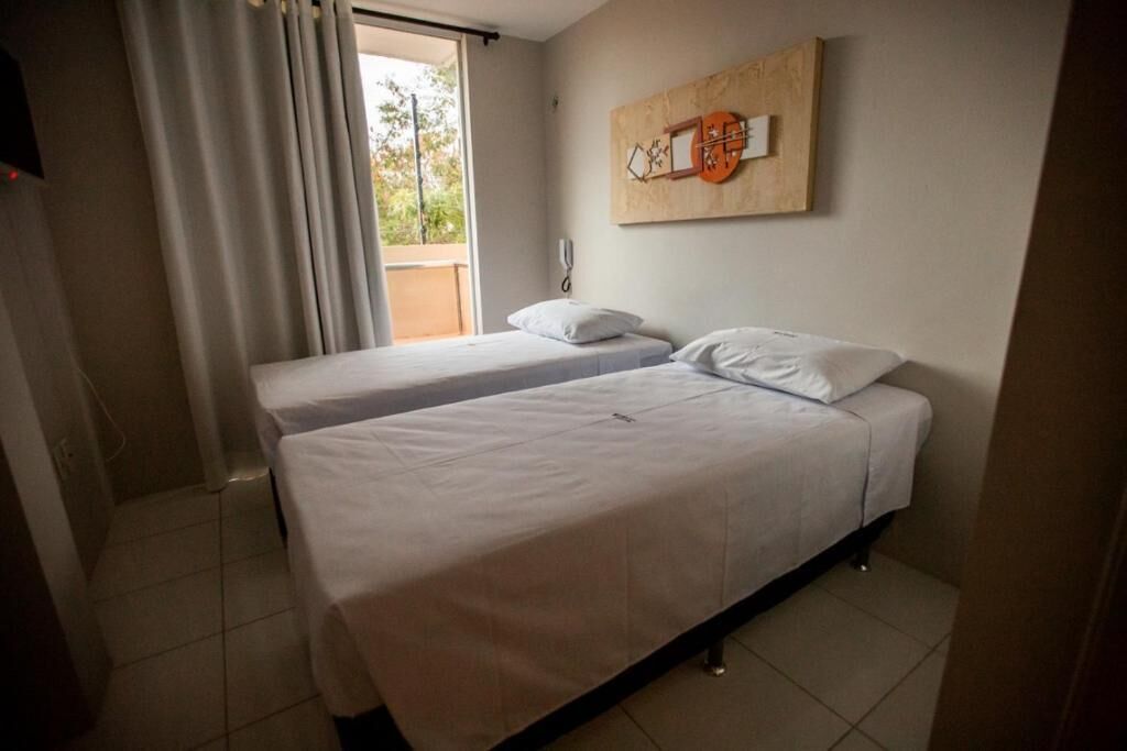 Une chambre d’hôtel avec deux lits simples, une fenêtre avec des rideaux, une œuvre d’art accrochée au mur et un téléphone.