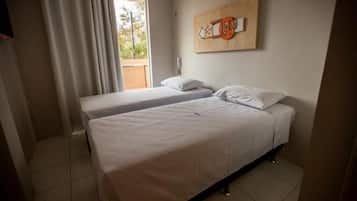 A hotel room with two single beds, a window with curtains, a wall-mounted artwork, and a telephone.