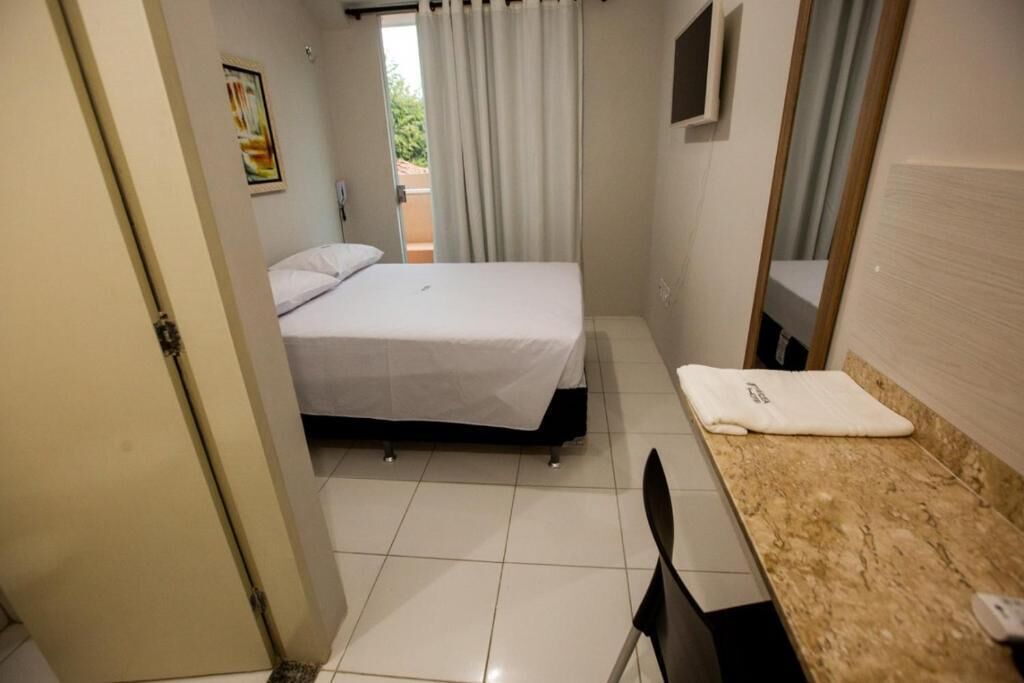 A small, clean room with a bed, a chair, a small table, and a window with curtains.