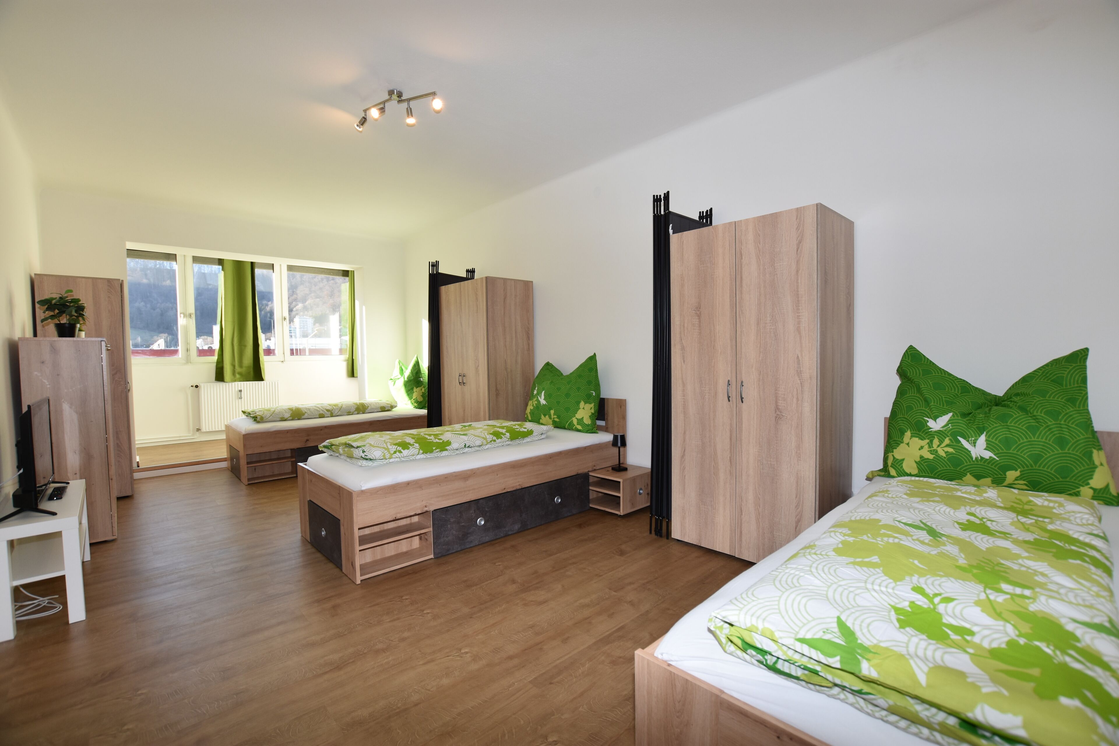 Ein modernes Schlafzimmer mit Holzboden, einem Bett mit grüner Bettwäsche, einer Bank, einem Kleiderschrank und einer Heizung.