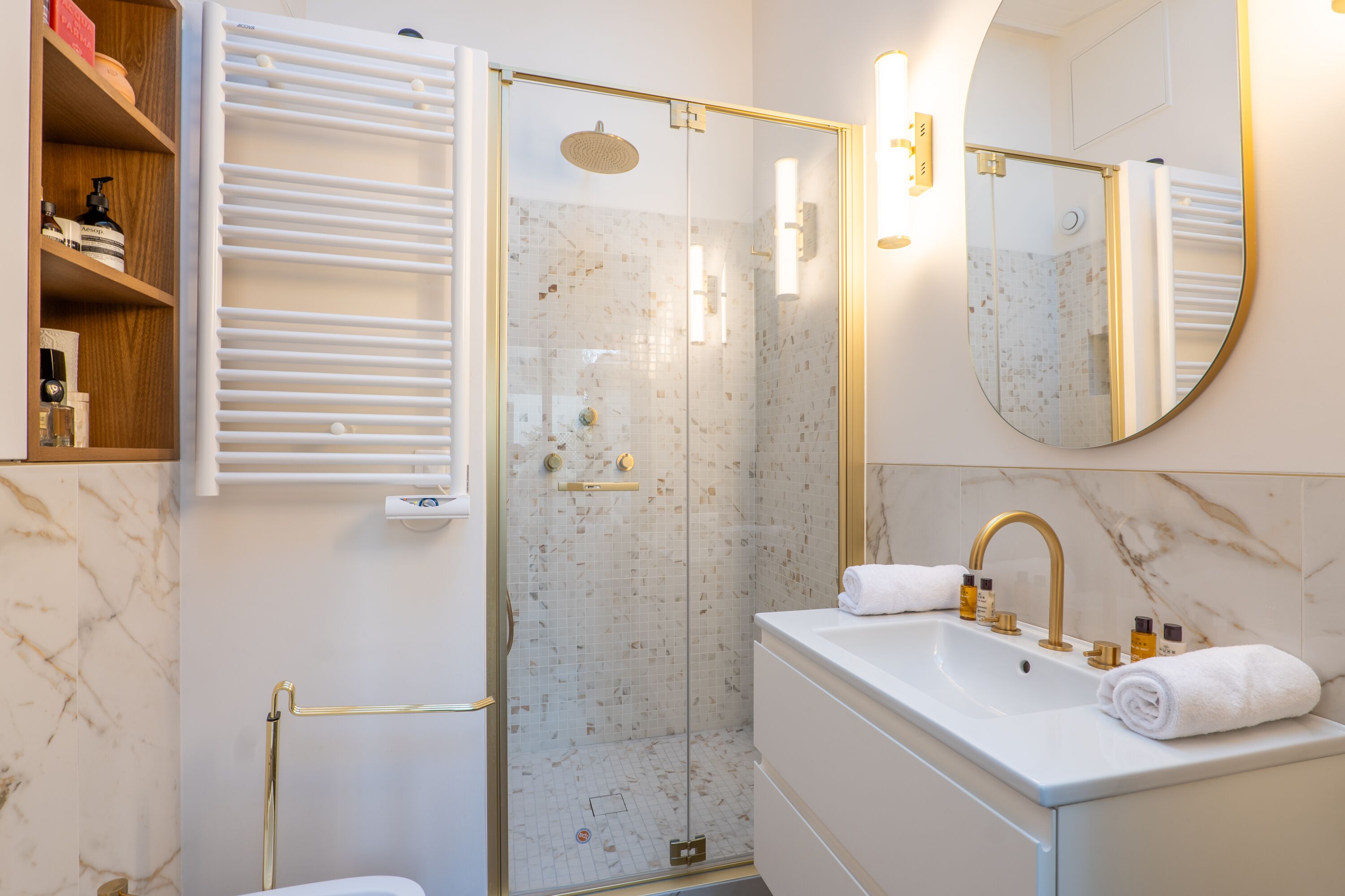 A modern bathroom with a glass-enclosed shower, a white sink with gold fixtures, and a marble-tiled wall.