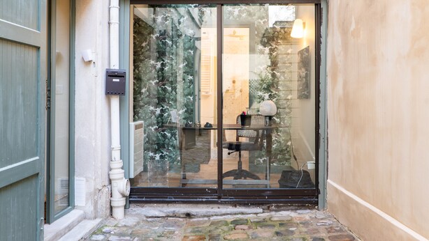 A glass door entrance with a small step leading up to it, a mailbox, and a chair outside. - A Story in Stone, by Veeve (Paris)