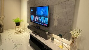 Un saló modern amb un gran televisor de pantalla plana muntat sobre una paret de marbre, un sòl de marbre, un moble de televisió negre i una petita planta en test.