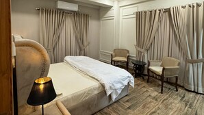 Habitació d'hotel amb un llit, un ventilador de sostre, un aparell d'aire condicionat, una taula amb cadires i cortines.