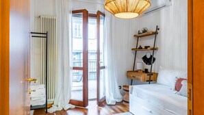Een hotelkamer met een bed, nachtkastjes, een hanglamp, een raam met gordijnen en uitzicht op het balkon.