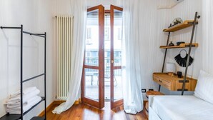 Een slaapkamer met een houten vloer, een bed, een kledingkast, een bureau en een raam met gordijnen.