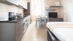 Una habitación de hotel compacta con kitchenette, zona de comedor, cama y televisor.