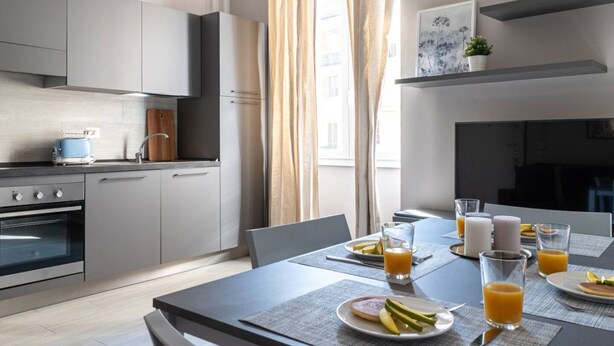 Una cocina moderna con gabinetes grises, un horno empotrado y un comedor con una mesa lista para el desayuno.