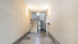 Un couloir étroit avec un escalier menant à l’étage supérieur. Les murs sont texturés et deux appliques murales y sont fixées.