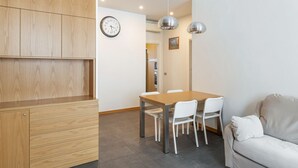 Une pièce moderne avec un meuble en bois, une table à manger avec des chaises, un canapé blanc, une horloge et des lampes suspendues.