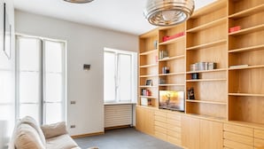 Un salon moderne avec un canapé beige, une bibliothèque en bois et une grande fenêtre.