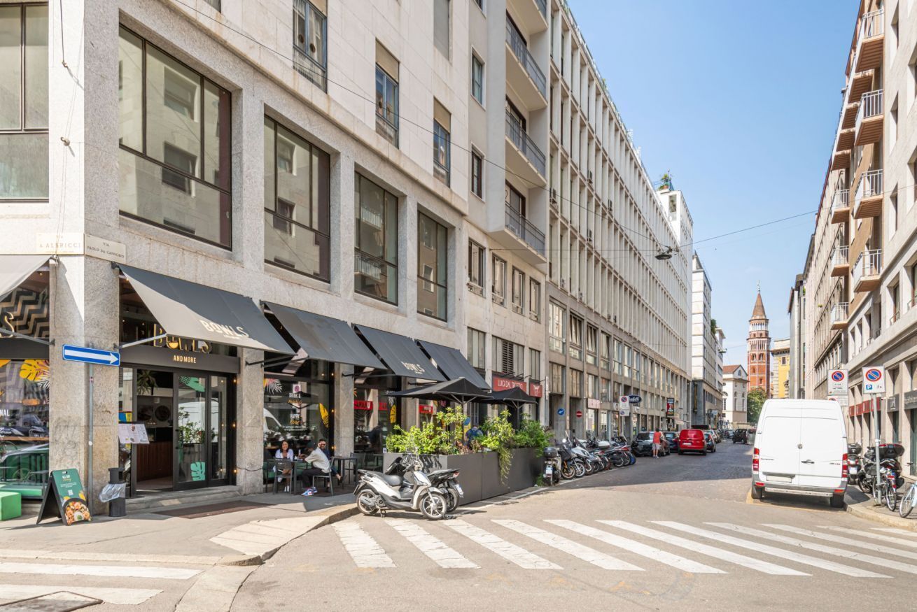 A street view with a row of buildings, a crosswalk, parked scooters, and a white van.