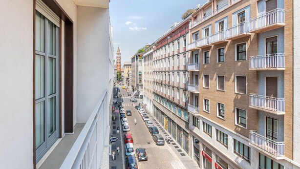Un immeuble à plusieurs étages doté de balcons, une rue bordée de voitures garées et un ciel dégagé.