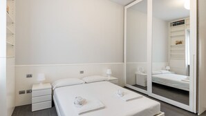 Une chambre d’hôtel moderne avec un grand lit, deux tables de chevet, un miroir et une armoire.