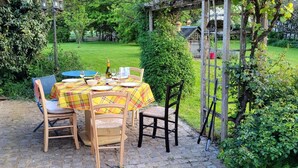 Een buitenterras met een tafel voor vier personen, omringd door stoelen, in een tuin met een pergola.