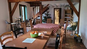 Een gezellig eetgedeelte met een houten tafel, stoelen en een geruit tafelkleed. Een kerstboom en een kleine kar met lichtjes zijn zichtbaar op de achtergrond.