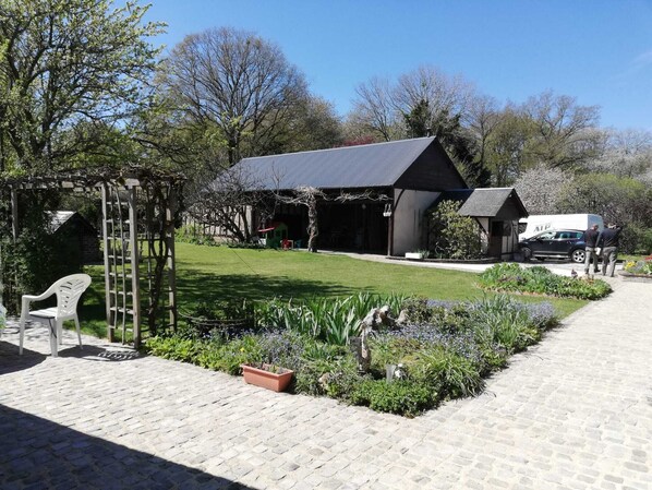 A garden with a pergola, a small shed, and a building with a sloped roof.
