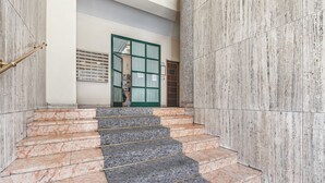 A staircase with alternating marble and stone steps, leading to a door with a green frame and a vent above it.