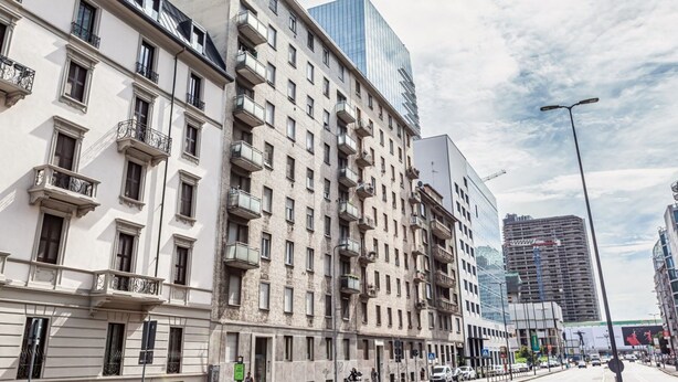 A multi-story building with balconies, a modern glass structure, and a construction site in the background.