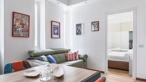 A modern living room with a wooden dining table, green sofa, and a bed in the adjacent room.