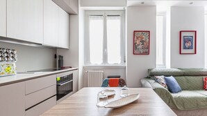 A modern kitchen with white cabinets, a dining table with glassware, and a green sofa in the living area.