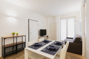 Uma sala de jantar com uma mesa posta para quatro pessoas, uma televisão e um sofá.
