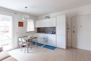 A compact kitchen with white cabinetry, a dining area with a table and chairs, a hanging light fixture, and a view of the outside balcony. - Easylife - Modern apt with terrace in Paolo Sarpi (Milano)