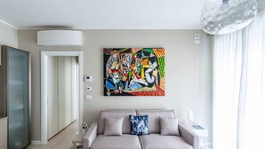 Un soggiorno moderno con un divano beige, un quadro astratto dai colori vivaci e un mobiletto in vetro.