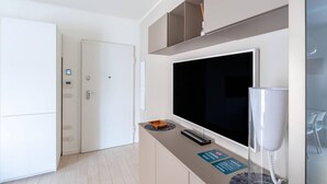 Una camera d'hotel moderna con una grande TV a schermo piatto, una scrivania con il telefono e una porta che dà su un'altra stanza.