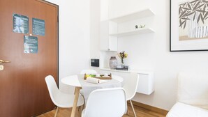 A modern room with a wooden door, a white dining table with chairs, a white shelf with decorative items, and a framed picture on the wall. - Easylife - Magic flat in Duomo (Milano)