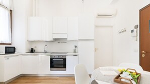 A compact kitchen with white cabinets, a microwave, a stove, and an oven. There's a dining table with a tray of tulips and a book. - Easylife - Magic flat in Duomo (Milano)