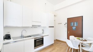A compact kitchen with white cabinets, a sink, a stove, and a small dining area with a table and chairs. - Easylife - Magic flat in Duomo (Milano)