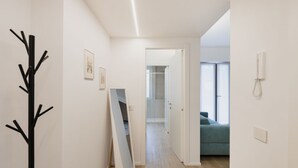 Un pasillo con un perchero, un espejo grande apoyado en la pared y una puerta que da a una habitación con un sofá azul.