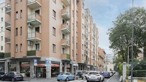 Un edificio residencial de varios pisos con balcones, una señal de estacionamiento y una calle con automóviles estacionados.