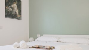 Habitación de hotel con cama, toallas blancas, una bandeja con tazas de té y un cuadro en la pared.
