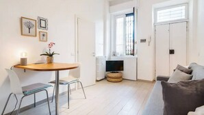 Un espacio habitable compacto con comedor, sofá, televisor y ventana con persianas.