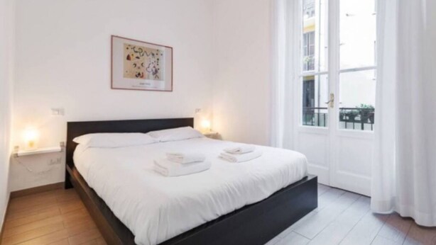 Un dormitorio moderno con una cama grande, ropa de cama blanca, una obra de arte enmarcada en la pared y una ventana con cortinas.