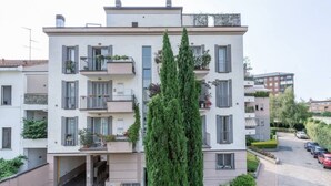 A multi-story residential building with balconies, a central entrance, and a parking area.