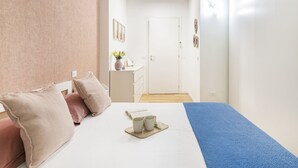Ein Schlafzimmer mit Bett, Kissen, einem Nachttisch mit Vase und Tablett mit Tassen sowie einer Tür zu einem anderen Raum.