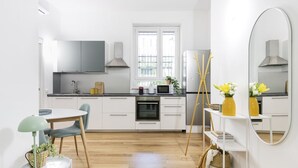 Eine moderne Küche mit weißen Schränken, einem eingebauten Ofen und einer Mikrowelle. Es gibt einen Essbereich mit Tisch und Stühlen, und einen großen Spiegel an der Wand.