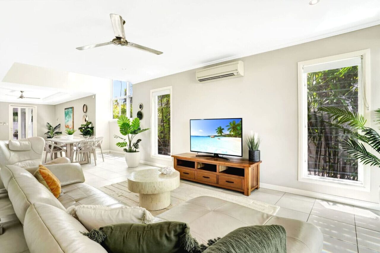 Una sala de estar moderna con un televisor de pantalla plana grande, un sofá, una mesa de centro y un comedor con sillas y plantas.
