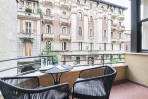 A balcony with wicker chairs and a table, overlooking a historic building with ornate balconies and windows.